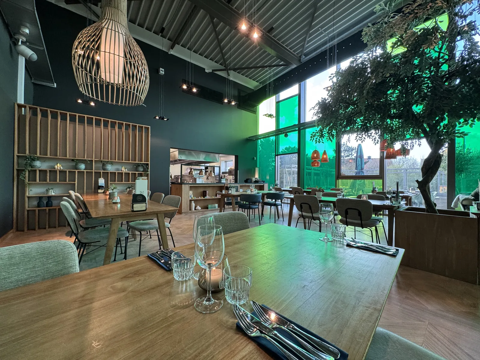 Restaurant von innen mit eingedecktem Holztisch, dunkelgrünen Wänden und Korbleuchten