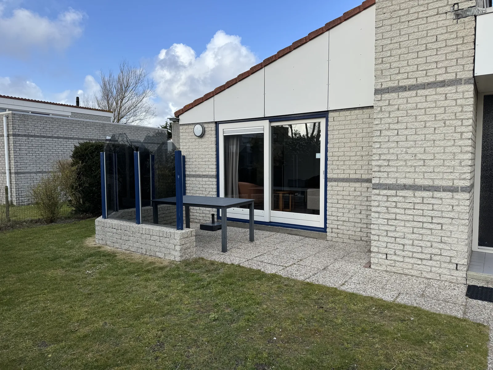 Rückseite eines Ferienhauses im Landal Beach Resort Ooghduyne mit überdachter Terrasse, Gartenmöbeln und Rasen