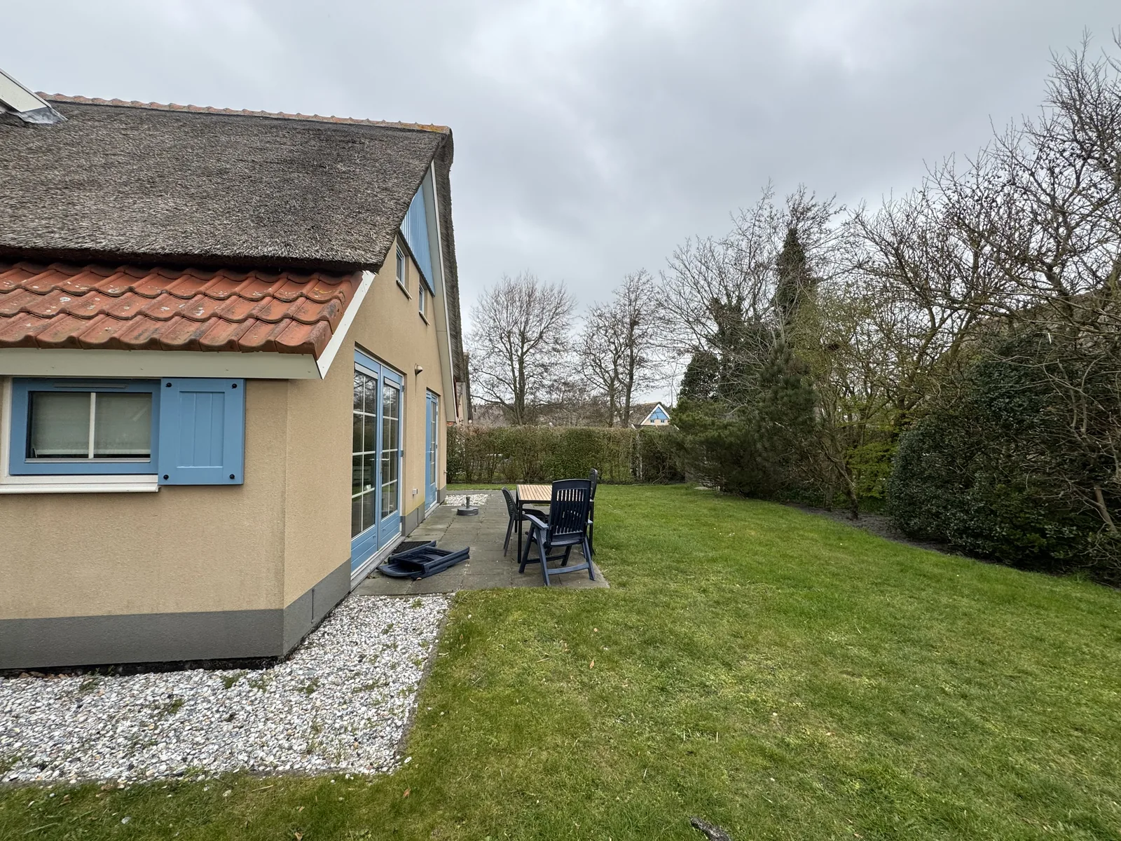 Ferienhaus mit blauen Fensterrahmen, Terrasse mit Gartenmöbeln und großem Rasen im Kustpark Texel
