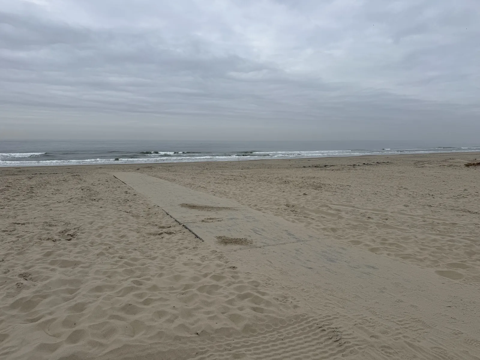 Sehr breiter, menschenleerer Sandstrand bei De Cocksdorp unter bedecktem Himmel, das Meer als schmaler Streifen am Horizont