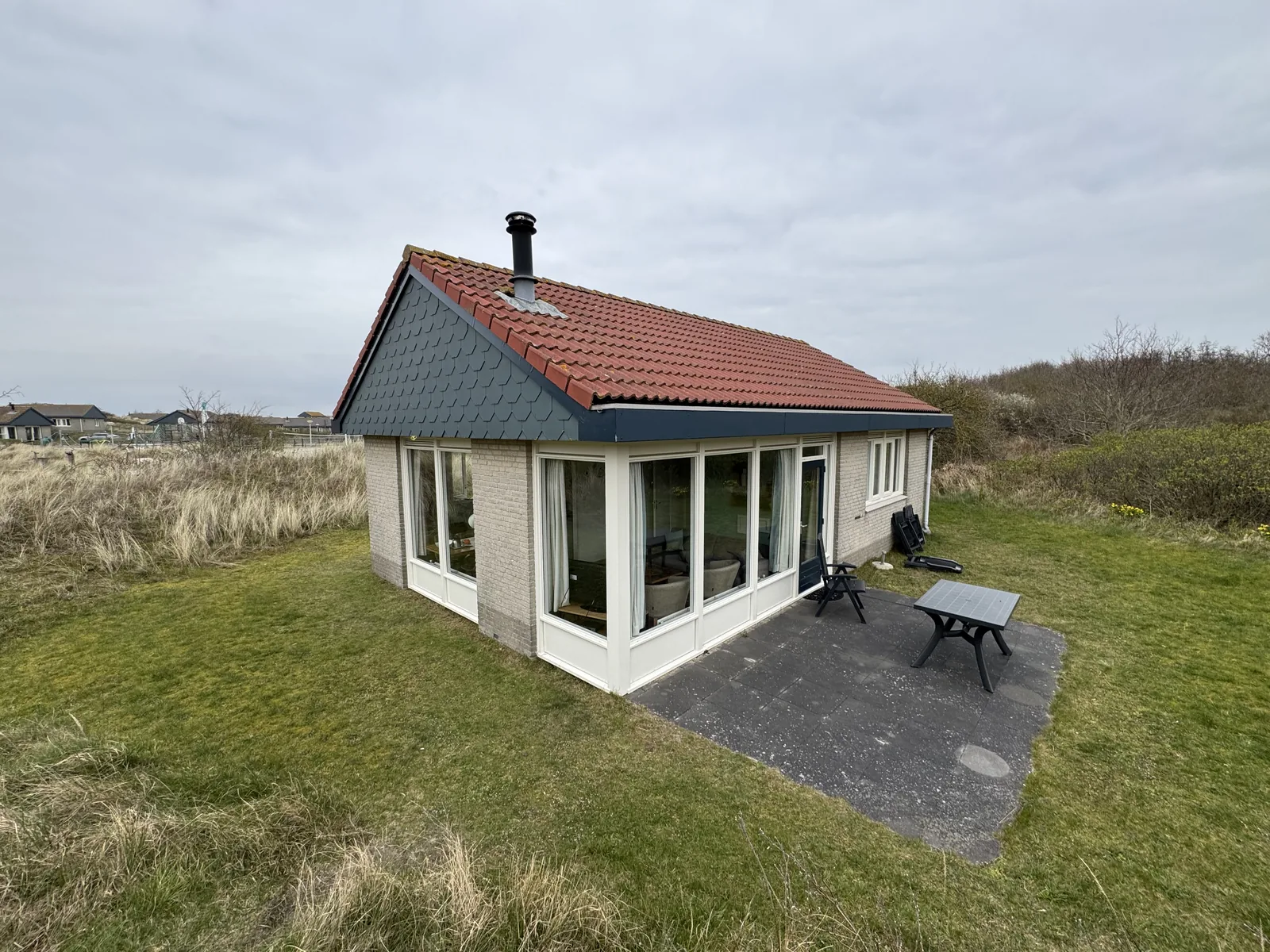 Ferienbungalow im Landal Sluftervallei mit umlaufender Fensterfront und gepflasterter Terrasse mit Tisch und Bank