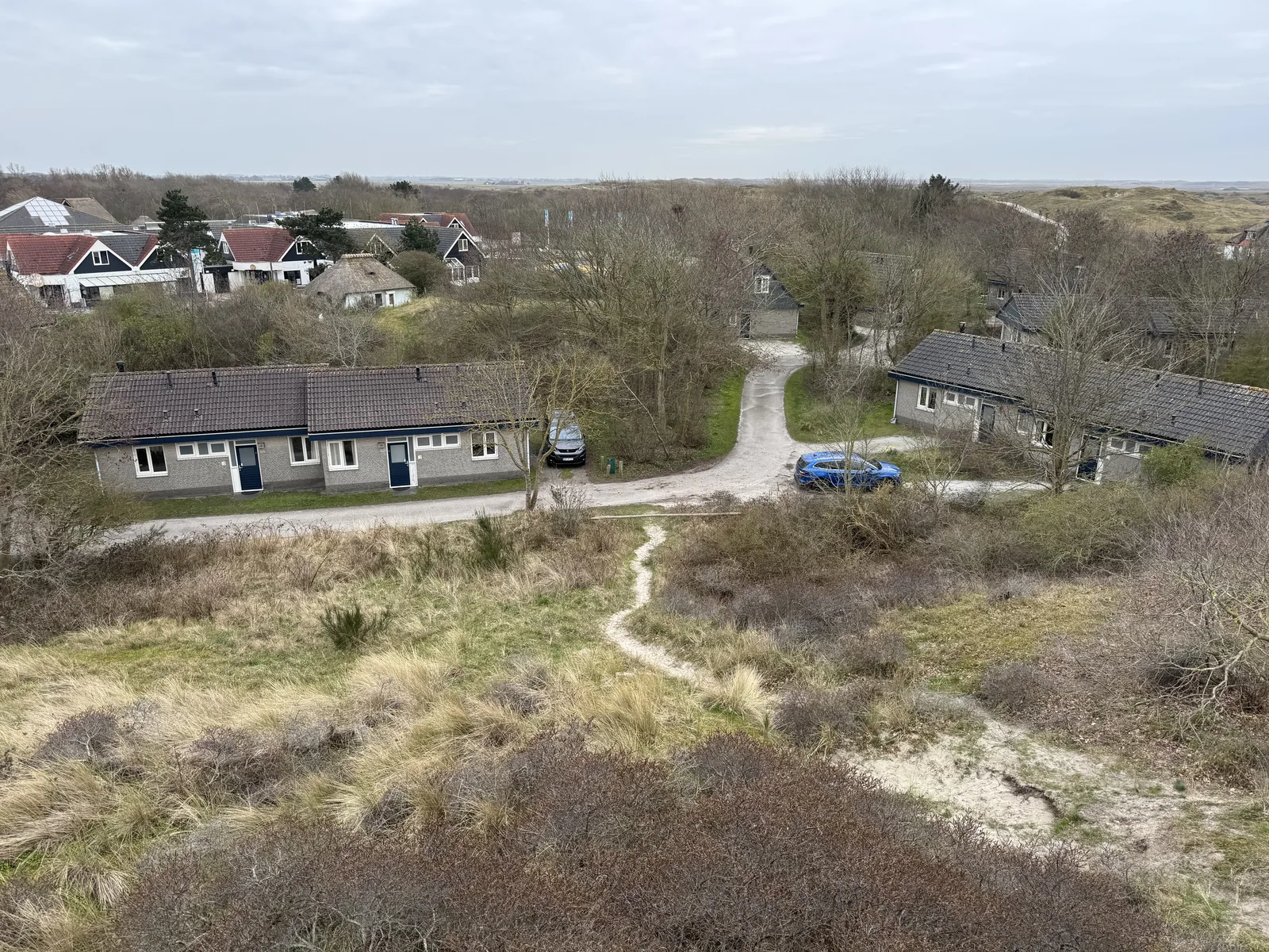 Erhöhter Blick auf eine langgestreckte Bungalowzeile im Landal Sluftervallei mit Parkplatz und Zufahrtsweg in der Dünenlandschaft