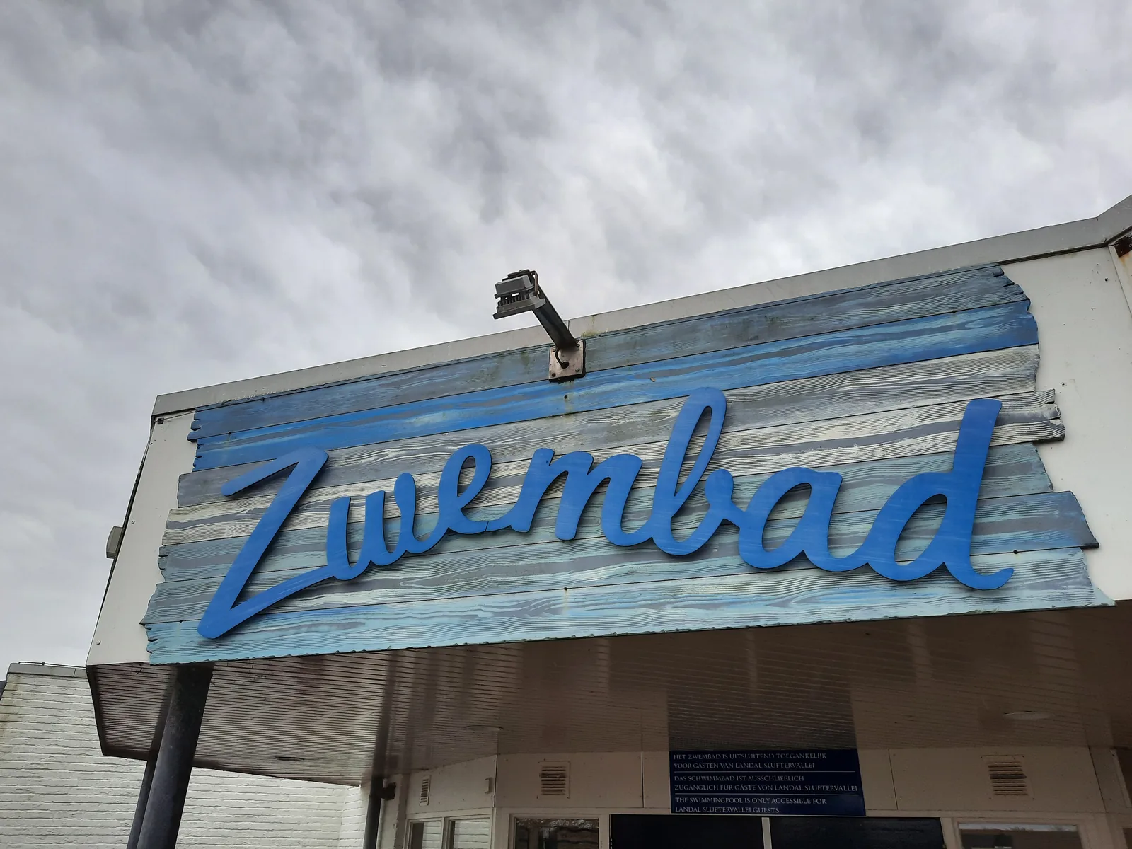 Gemaltes Holzschild mit dem Schriftzug Zwembad über dem Eingang des Hallenbads am Landal Sluftervallei