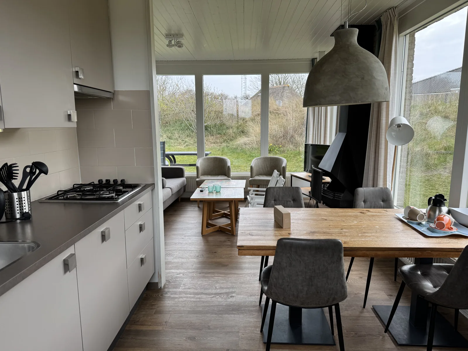 Wohnküche eines Bungalows im Landal Sluftervallei mit Gaskochfeld, Esstisch mit Stühlen und breiter Fensterfront ins Grüne