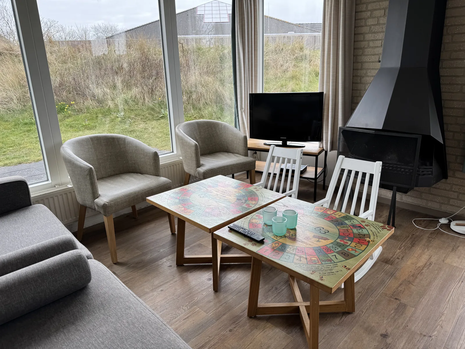 Wohnzimmer eines Bungalows im Landal Sluftervallei mit Kaminofen, Fernseher, Sesseln und niedrigem Couchtisch vor der Fensterfront