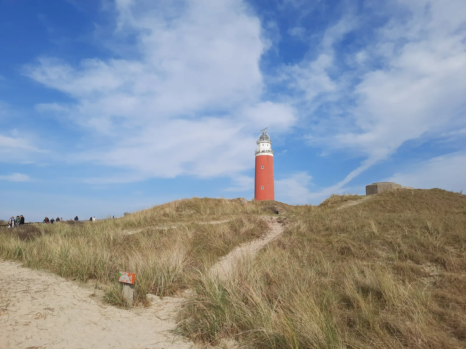 Der rot-weiße Leuchtturm auf der Dünenkuppe, ein Sandpfad führt hinauf