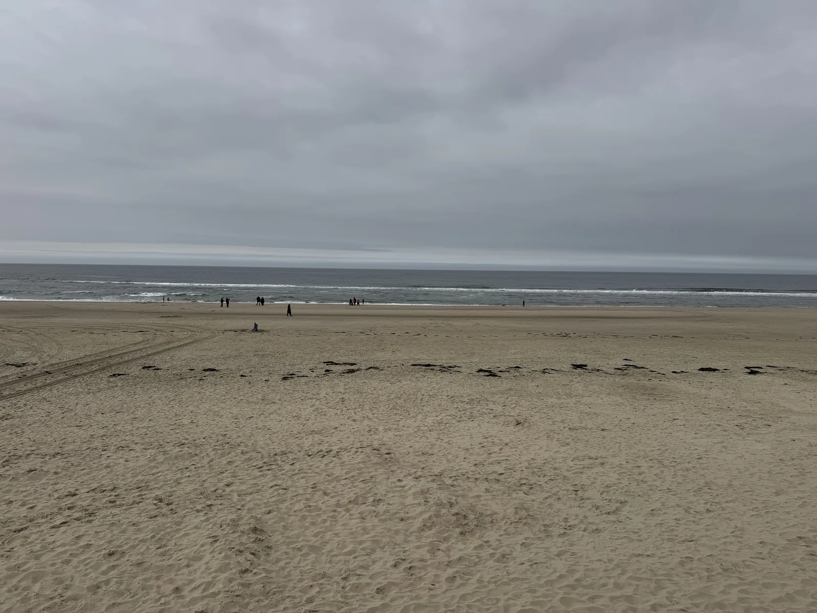 Weiter, fast menschenleerer Sandstrand unter grauem Himmel mit ruhiger Nordsee